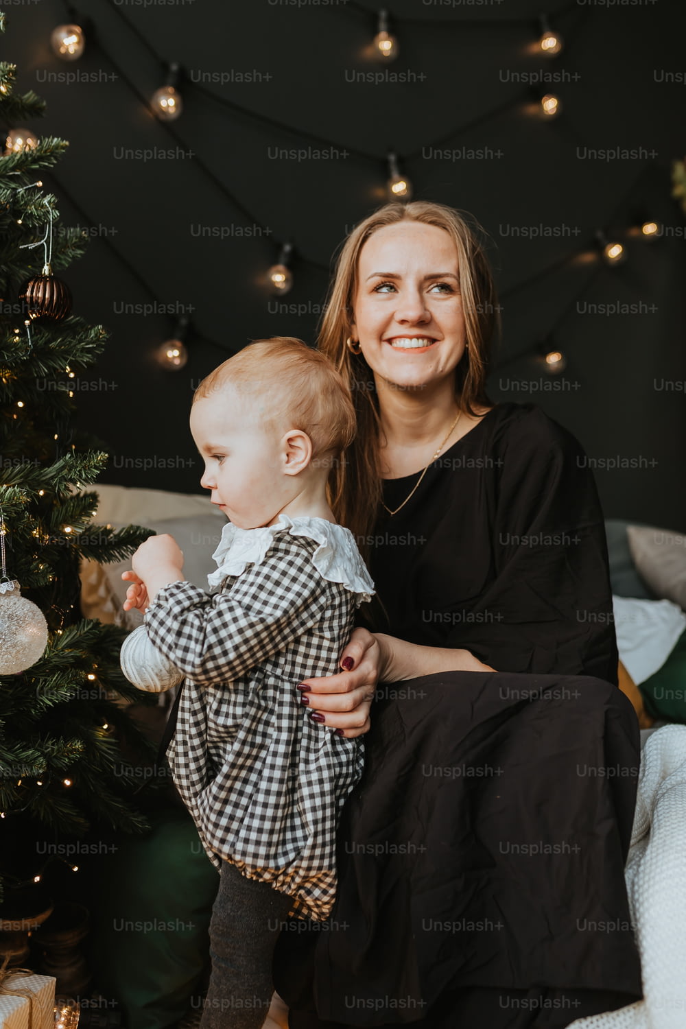 a woman holding a baby next to a christmas tree