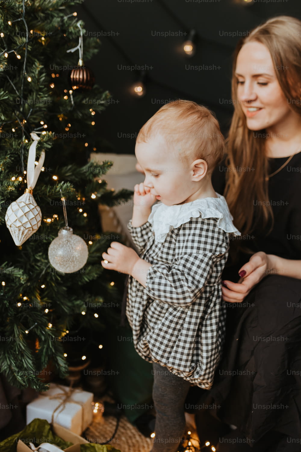 Una mujer sosteniendo a un bebé junto a un árbol de Navidad