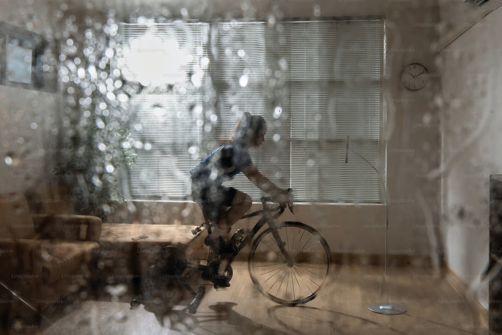 Ciclista donna asiatica. Si sta esercitando in casa. Pedalando sul trainer e giocando a giochi di bici online. Durante la stagione delle piogge