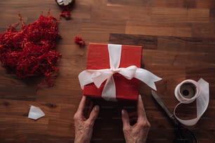 une personne tenant une boîte-cadeau rouge avec un ruban blanc