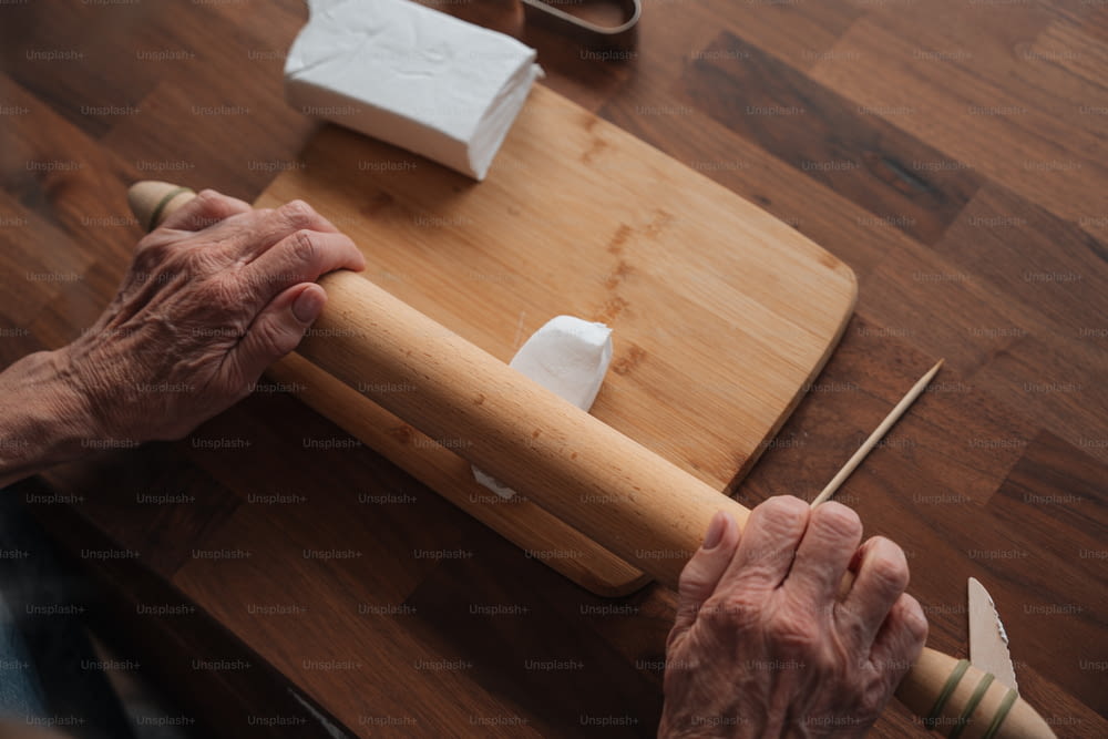 an older person holding a rolling pin on top of a wooden table