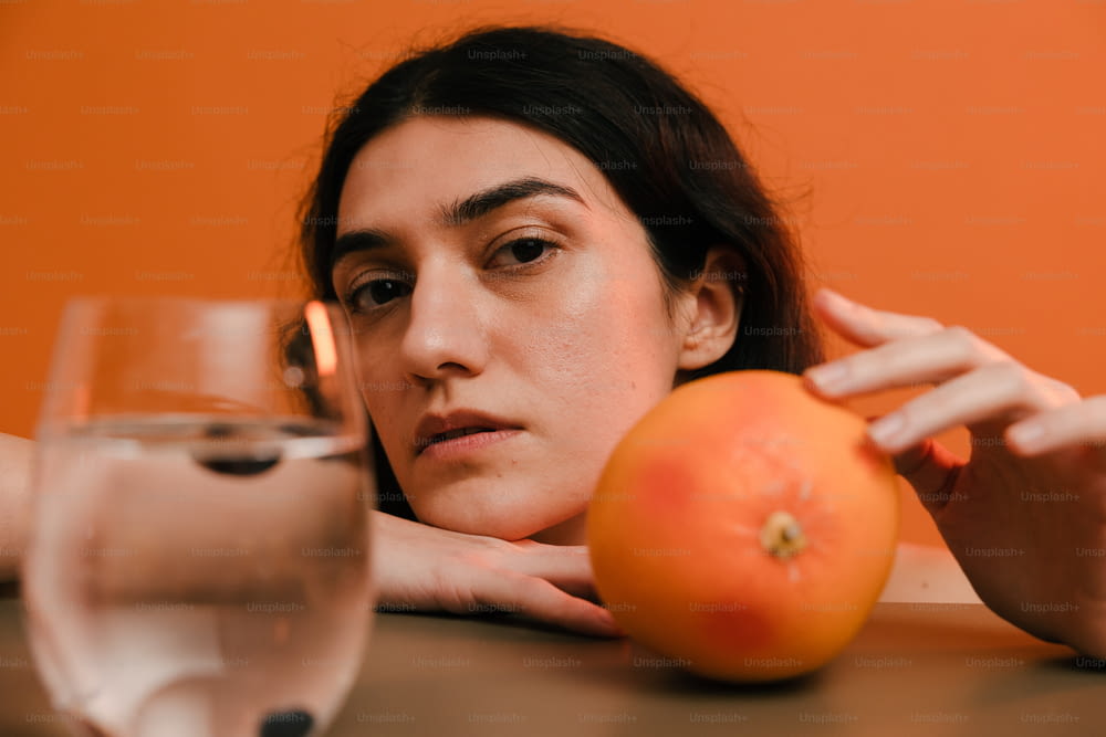Eine Frau sitzt an einem Tisch mit einer Orange und einem Glas Wasser