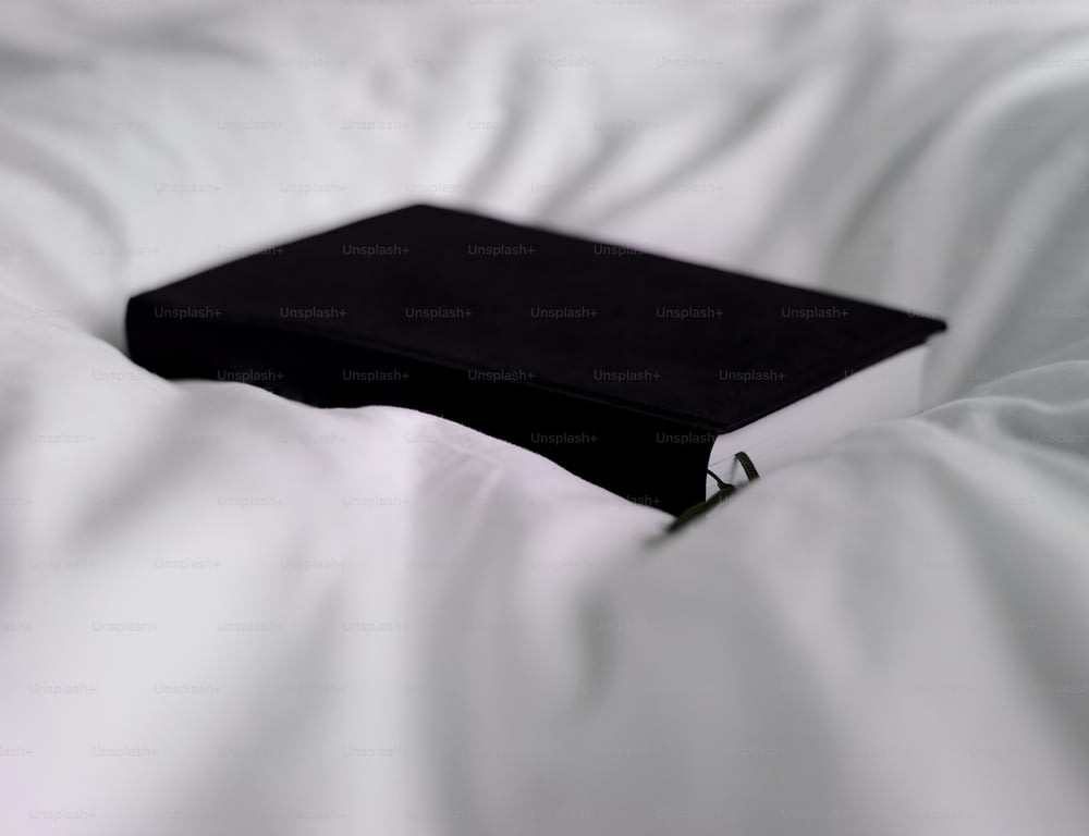 Un libro negro sentado encima de una cama blanca