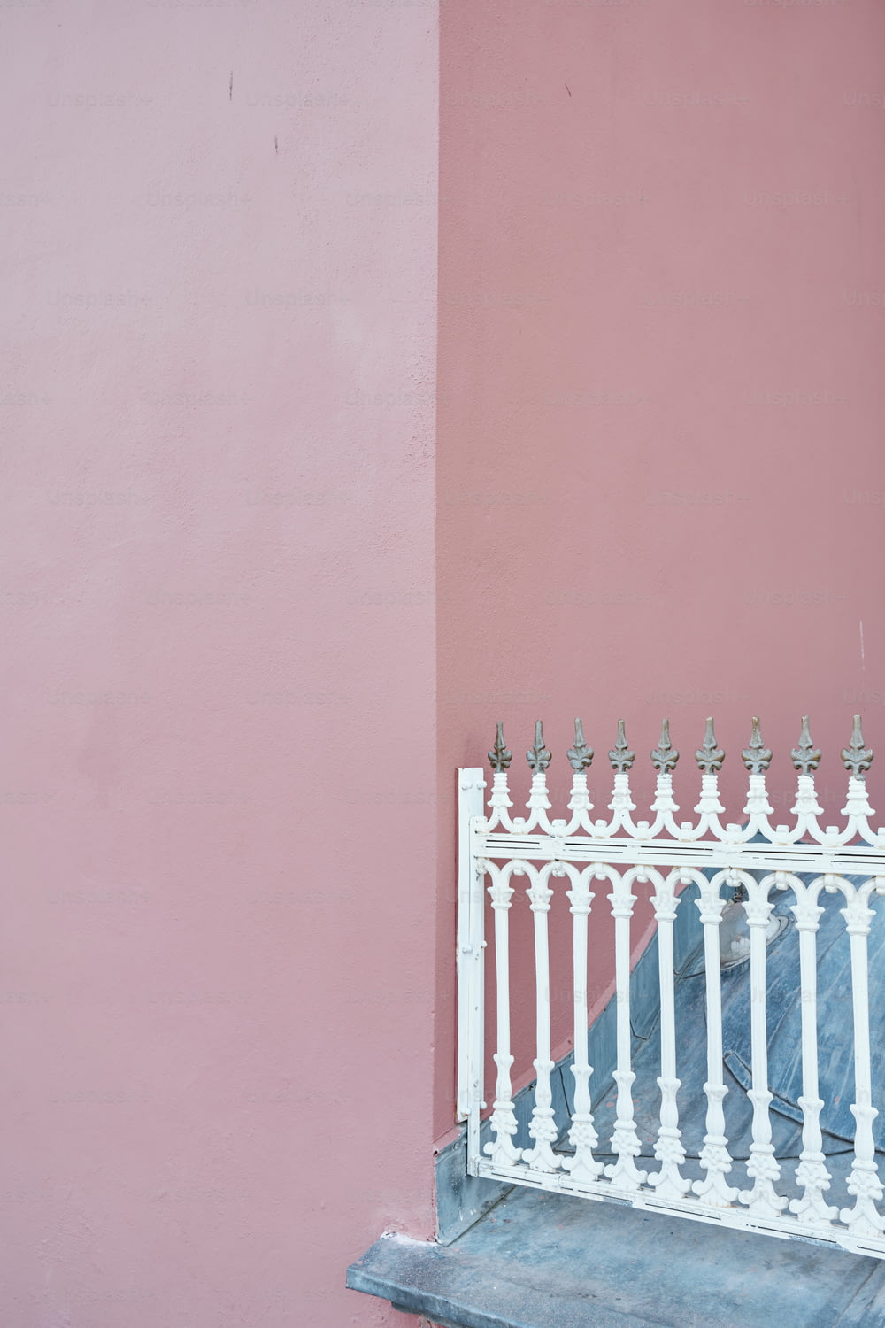 a white iron fence against a pink wall