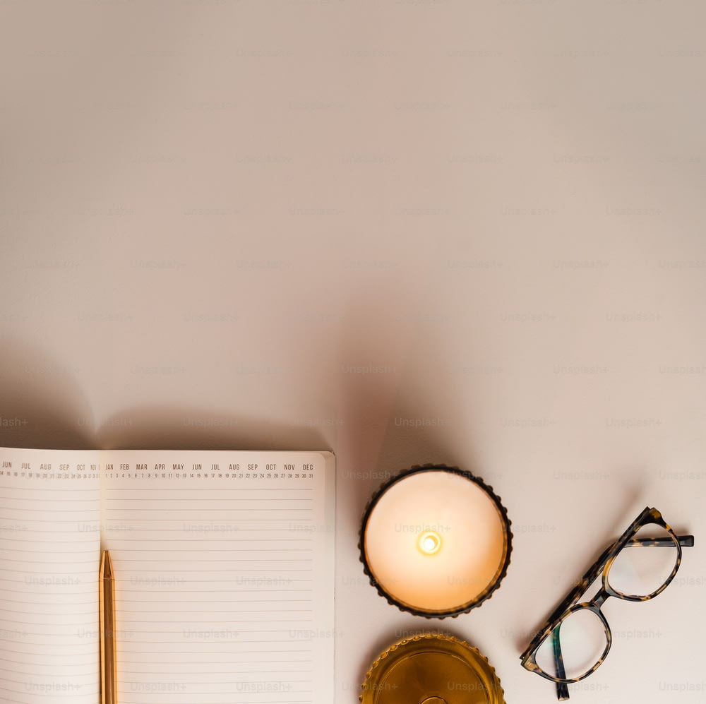 ein Schreibtisch mit Notizbuch, Stift, Brille und Kerze