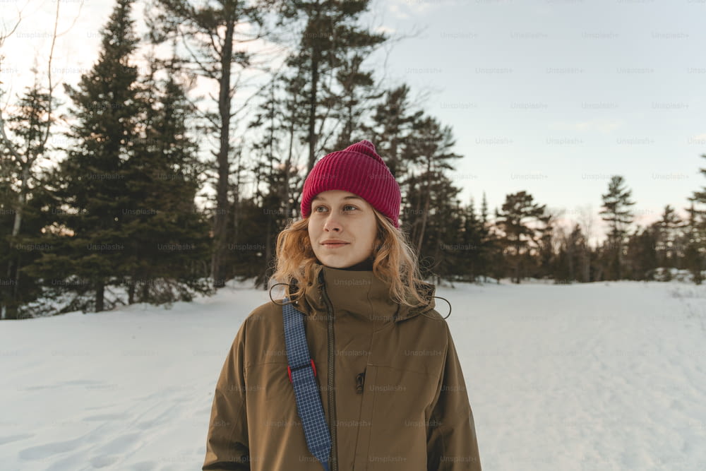 Una donna in piedi nella neve che indossa un cappello rosso