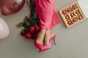 Die Füße einer Frau in rosa Schuhen neben einer Schachtel Bonbons