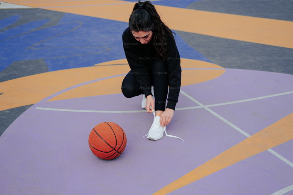 a woman tying a shoe on top of a basketball court