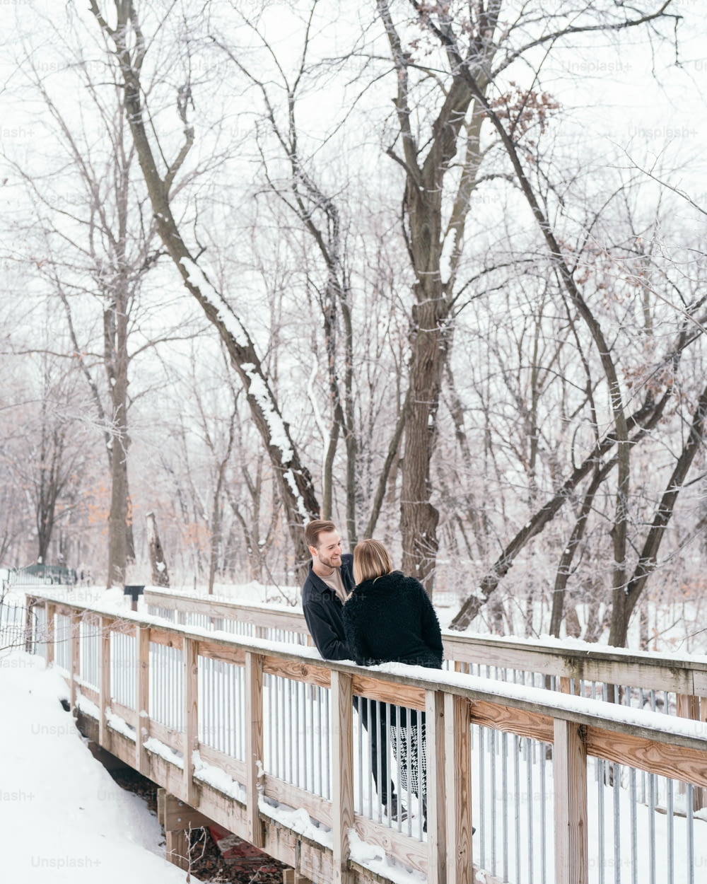 two people standing on a bridge in the snow