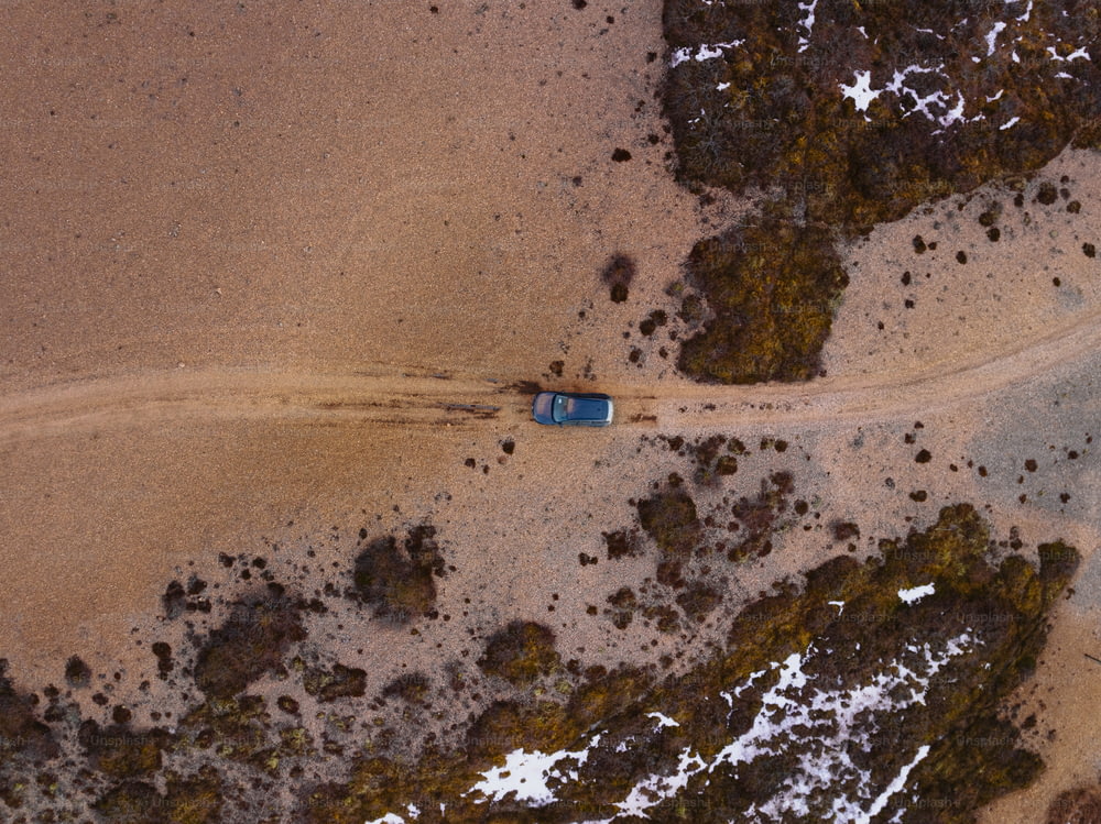 an aerial view of a car driving on a dirt road