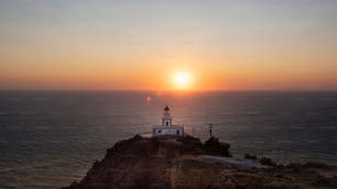 the sun is setting over a lighthouse on a cliff