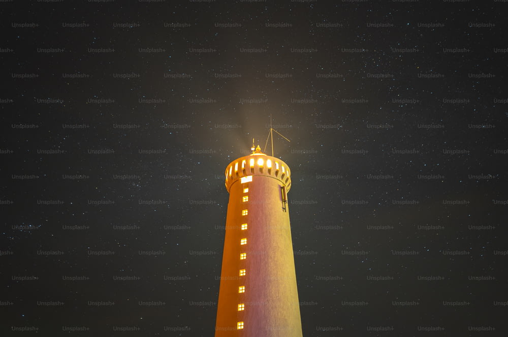 a light house lit up at night with stars in the sky