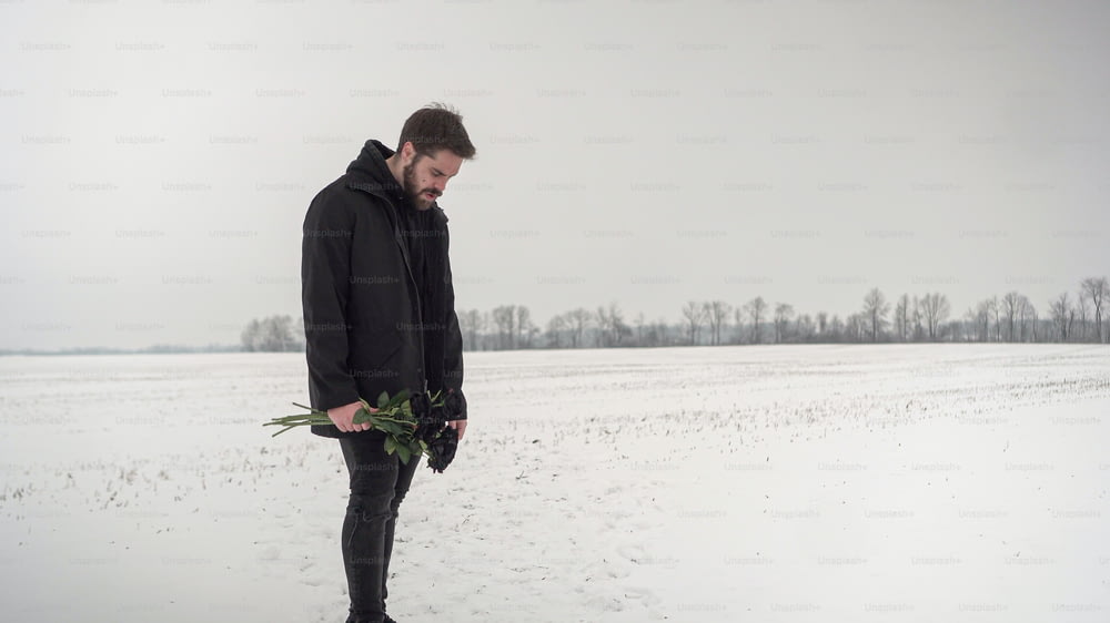 a man standing in the snow holding a bouquet of flowers