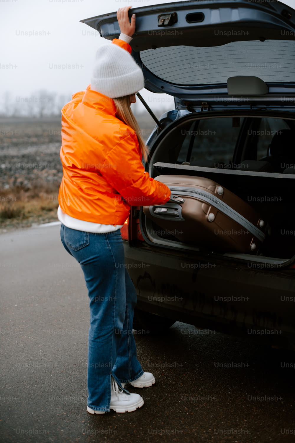 uma mulher em uma jaqueta laranja abrindo o porta-malas de um carro