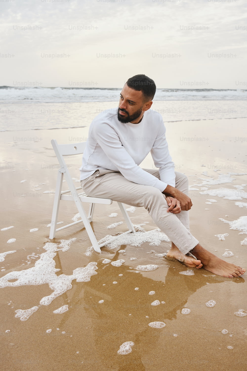 해변 꼭대기에 있는 하얀 의자 위에 앉아 있는 남자