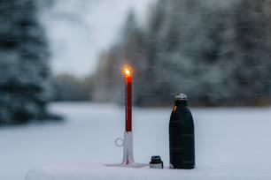 uma vela e uma garrafa em uma mesa na neve