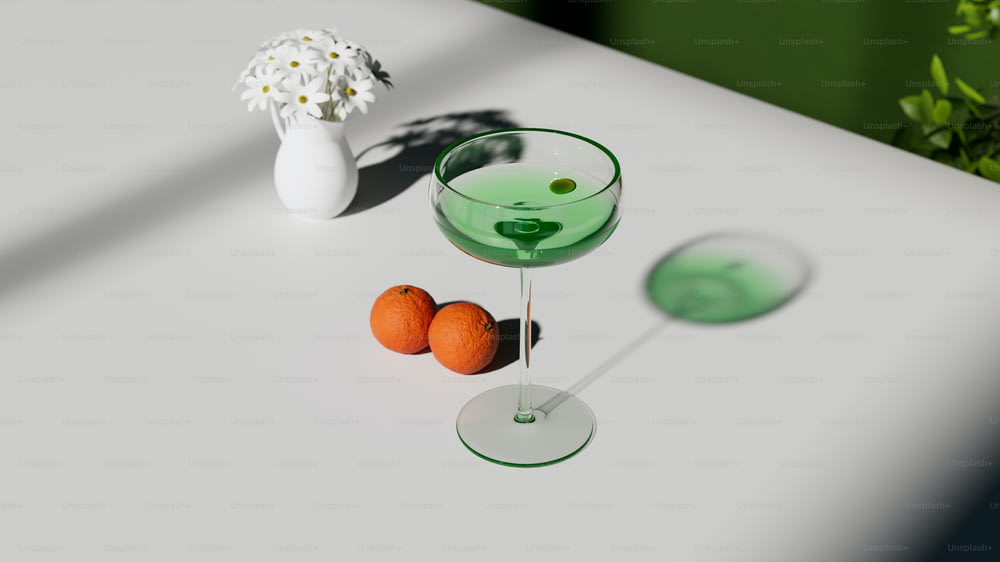 ein Glas grüne Flüssigkeit neben zwei Orangen