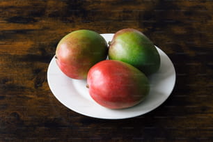 a white plate topped with three apples on top of a wooden table