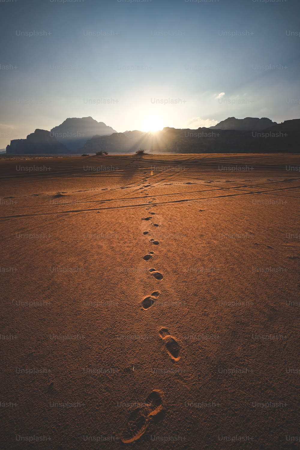 uma trilha de pegadas no deserto ao pôr do sol