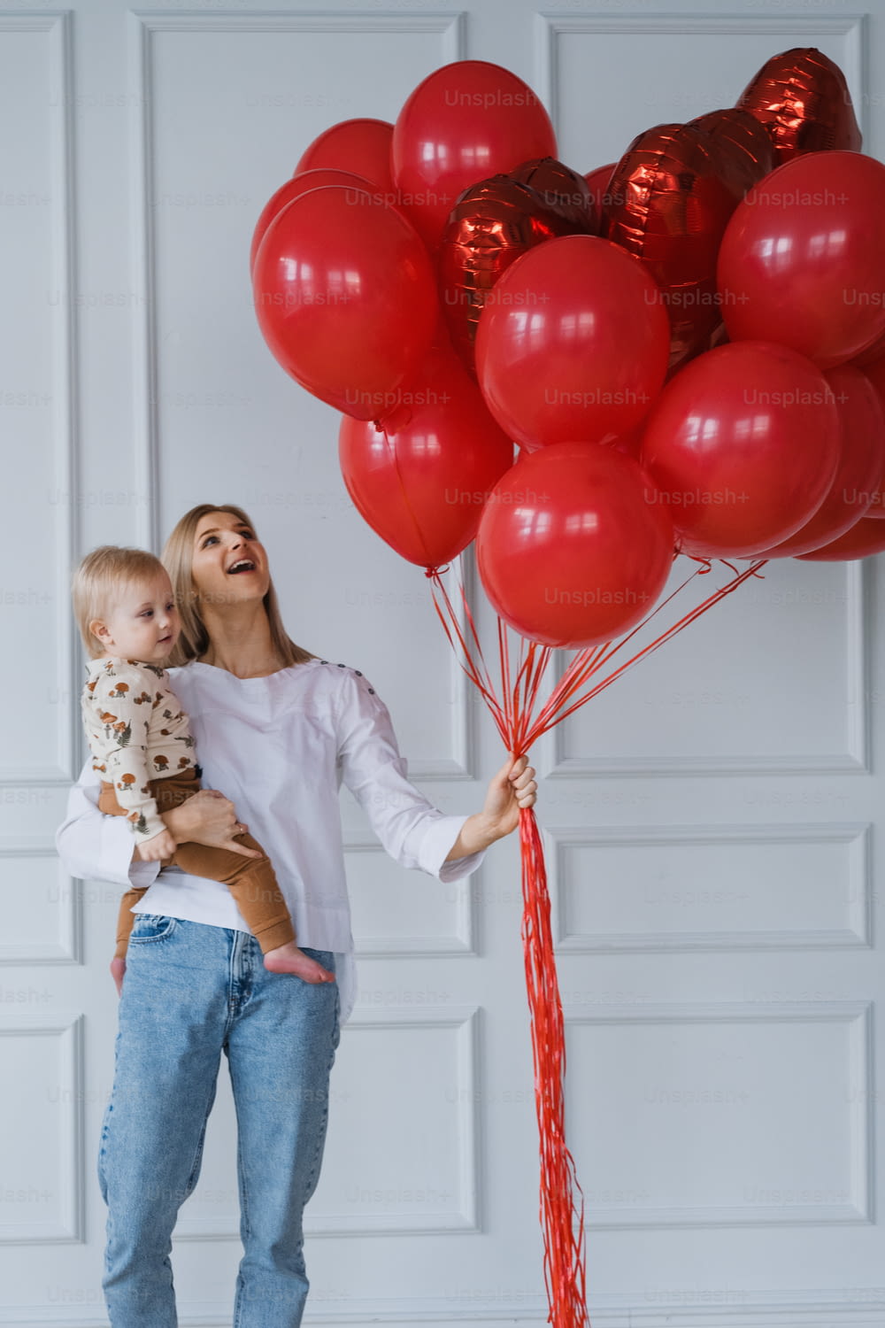 a woman holding a baby and a bunch of red balloons