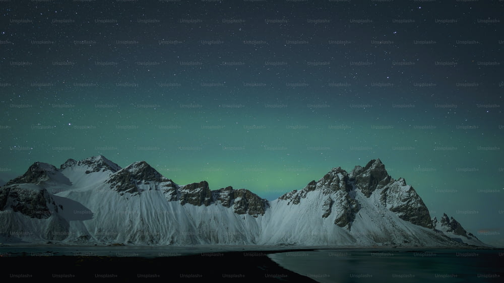 a snowy mountain range with a green light in the sky