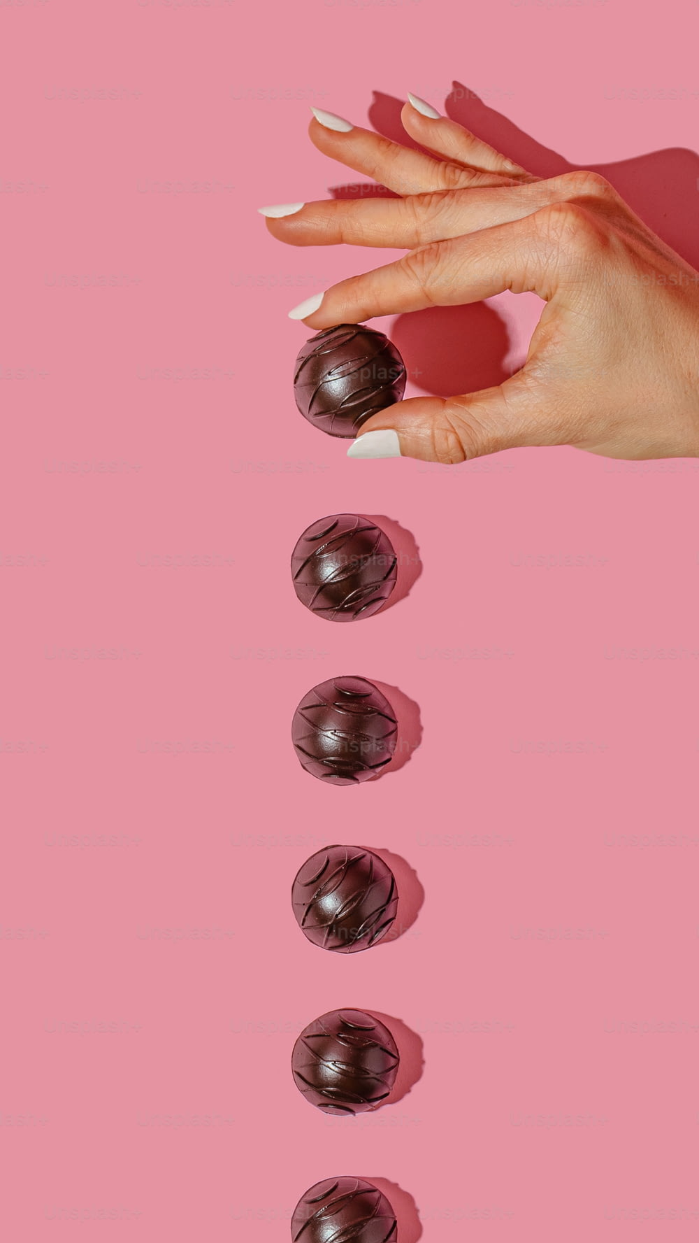 Una mano de mujer con manicura y chocolates sobre fondo rosa