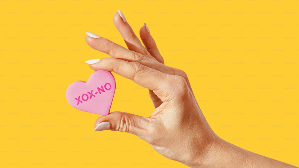 a mão de uma mulher segurando um biscoito rosa em forma de coração