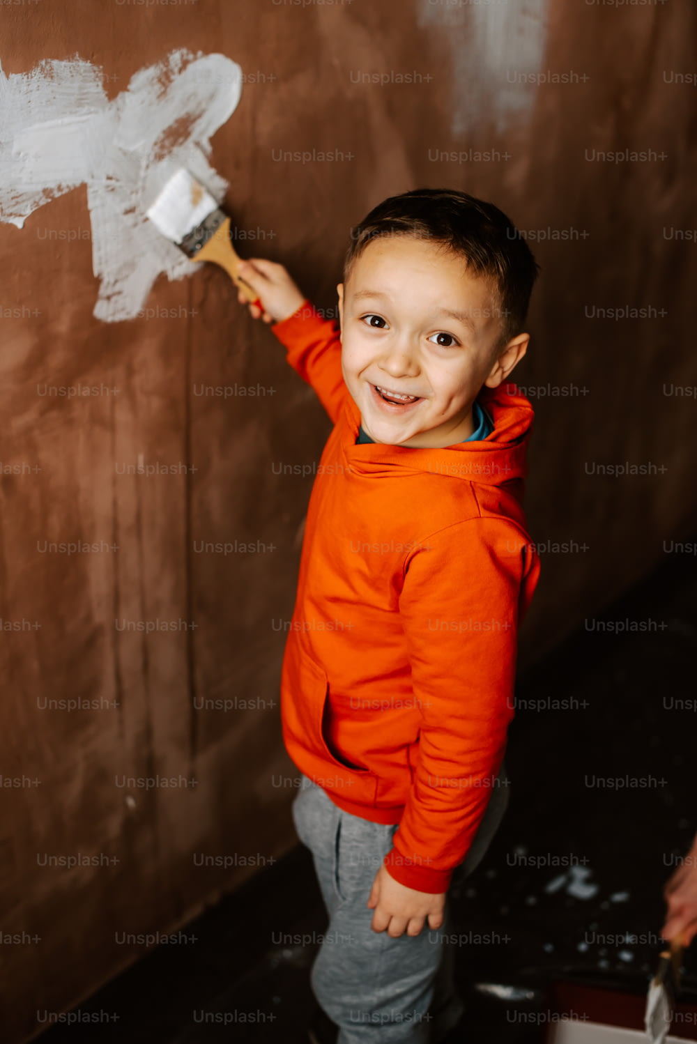 a young boy standing in front of a wall with a paintbrush
