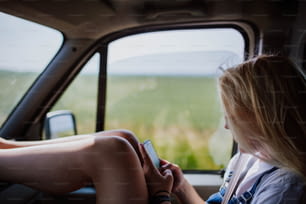 Una mujer sentada en un auto mirando su teléfono celular