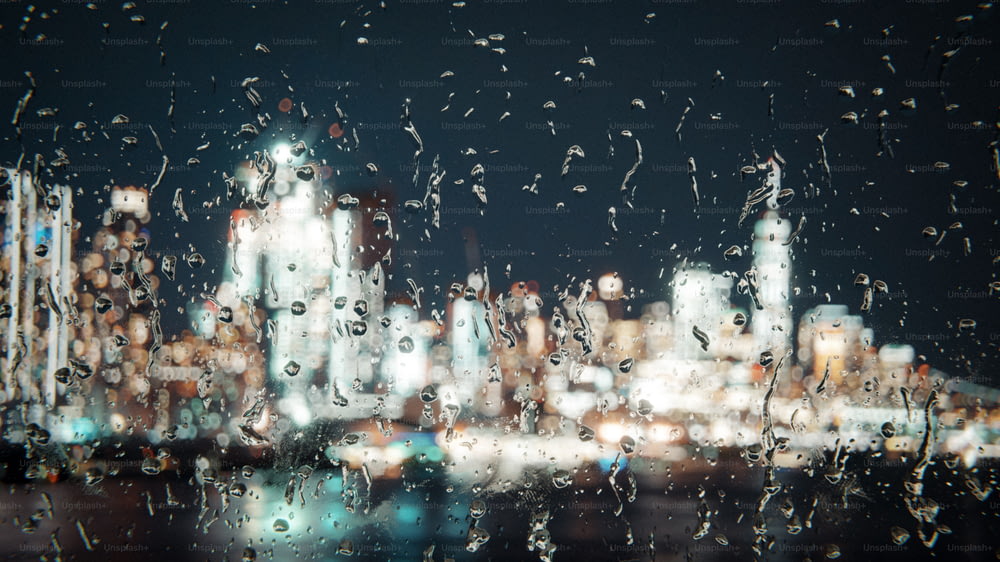 Una veduta di una città di notte attraverso una finestra coperta di pioggia