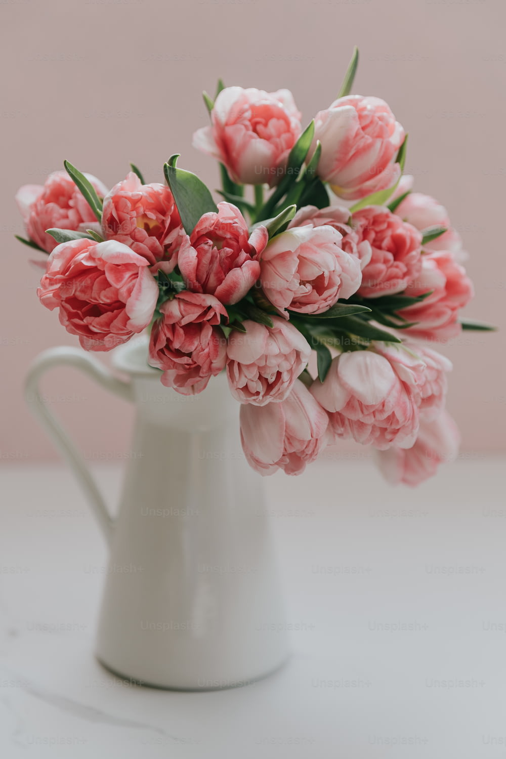 un vaso bianco pieno di fiori rosa in cima a un tavolo