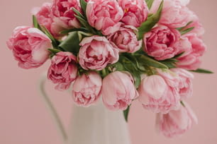 Un jarrón blanco lleno de flores rosadas encima de una mesa