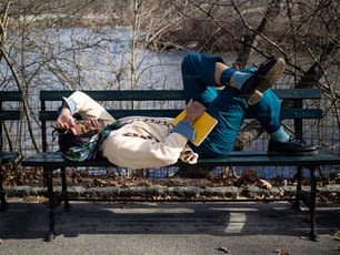 川のほとりの緑のベンチの上��に横たわる男