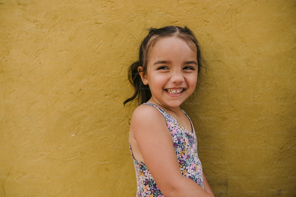 a little girl standing in front of a yellow wall