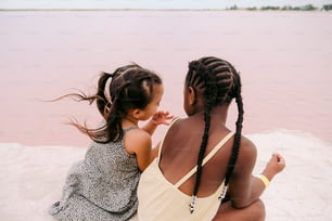 Zwei kleine Mädchen sitzen auf dem Sand in der Nähe eines Gewässers