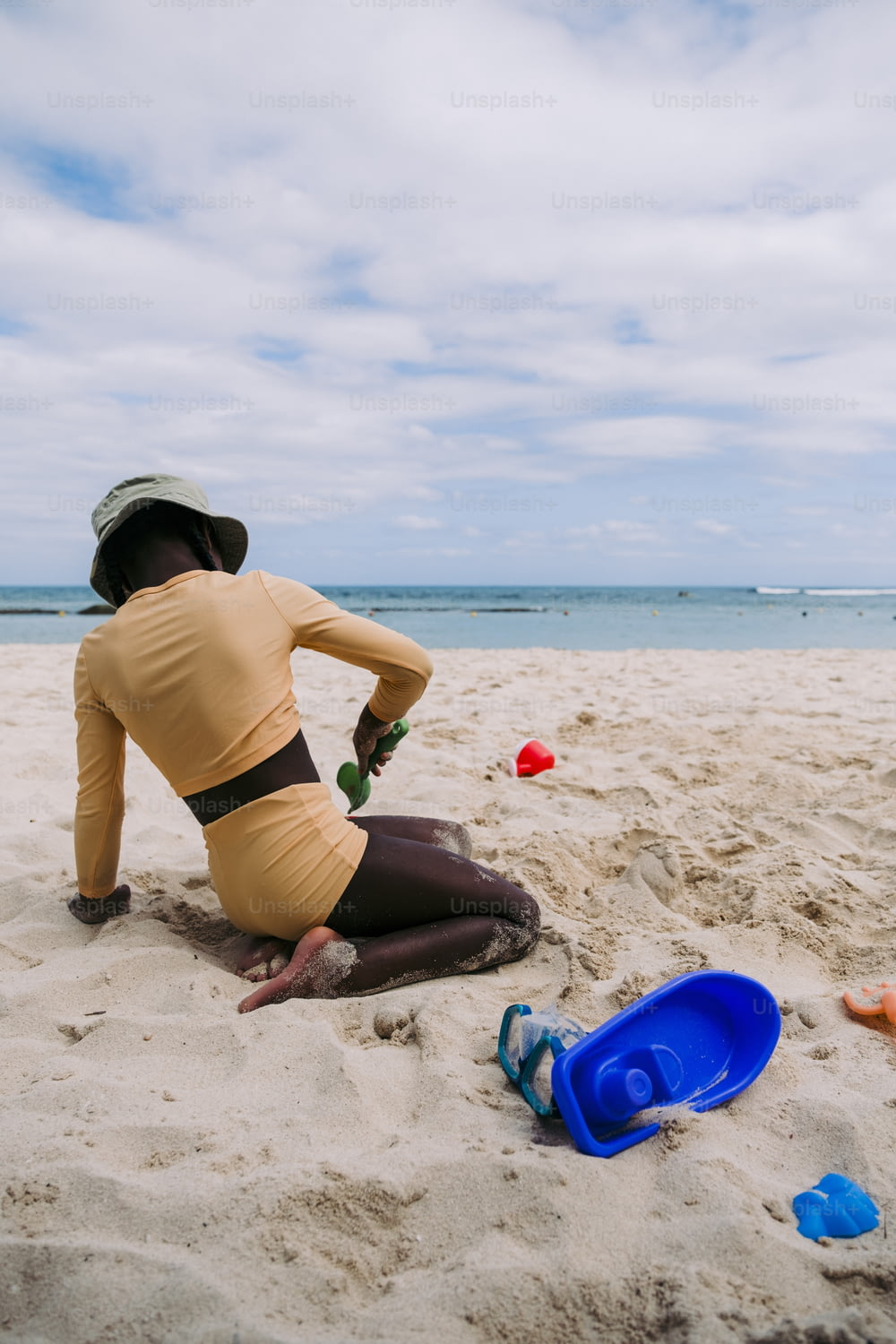 a woman sitting on a beach next to a blue frisbee