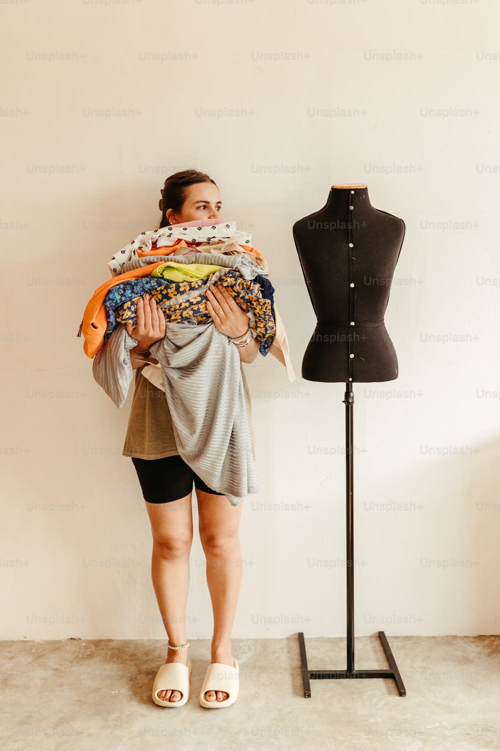 a woman holding a pile of clothes next to a mannequin