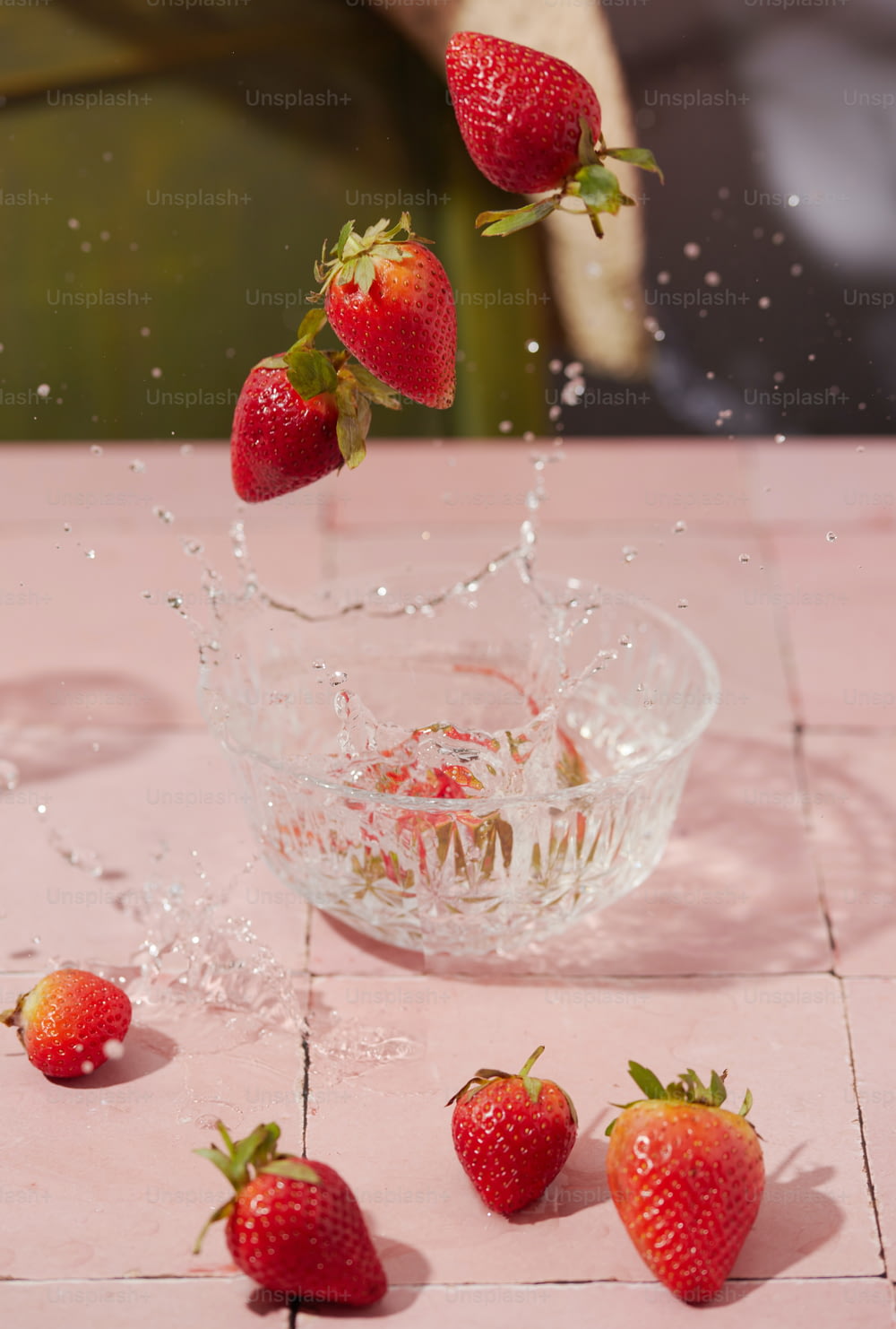 strawberries falling into a bowl of water on a table