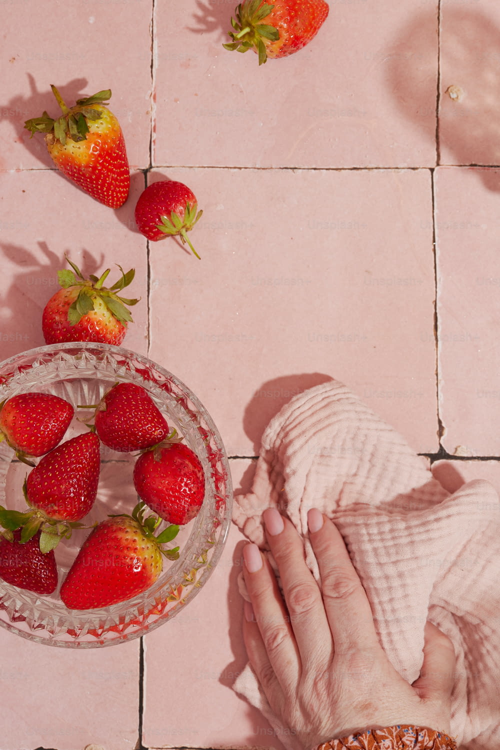 분홍색 타일 바닥에 딸기 한 그릇과 딸기 한 그릇