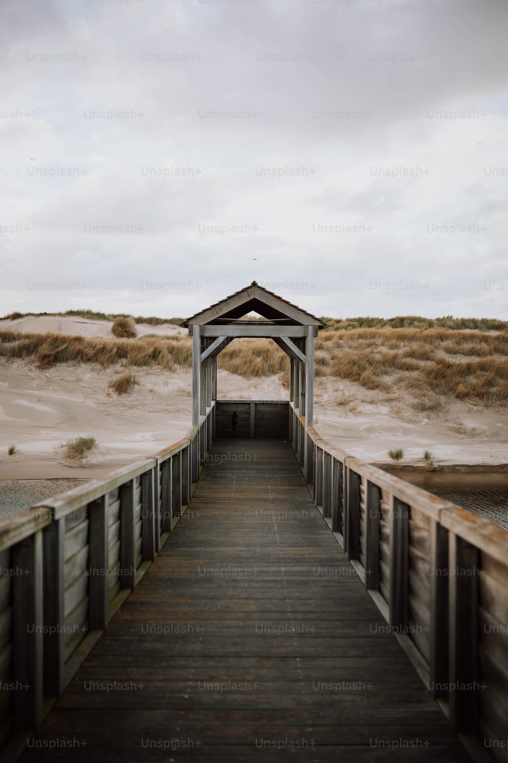 une passerelle en bois menant à une plage avec des dunes de sable en arrière-plan