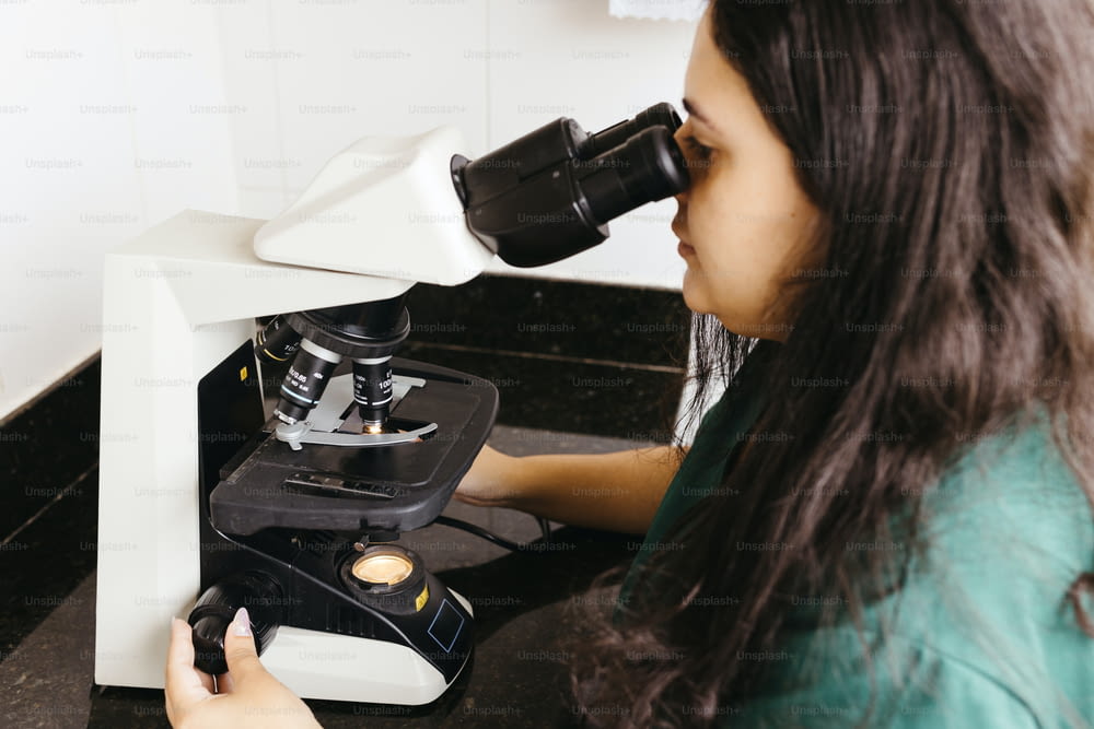 uma mulher olhando através de um microscópio para algo
