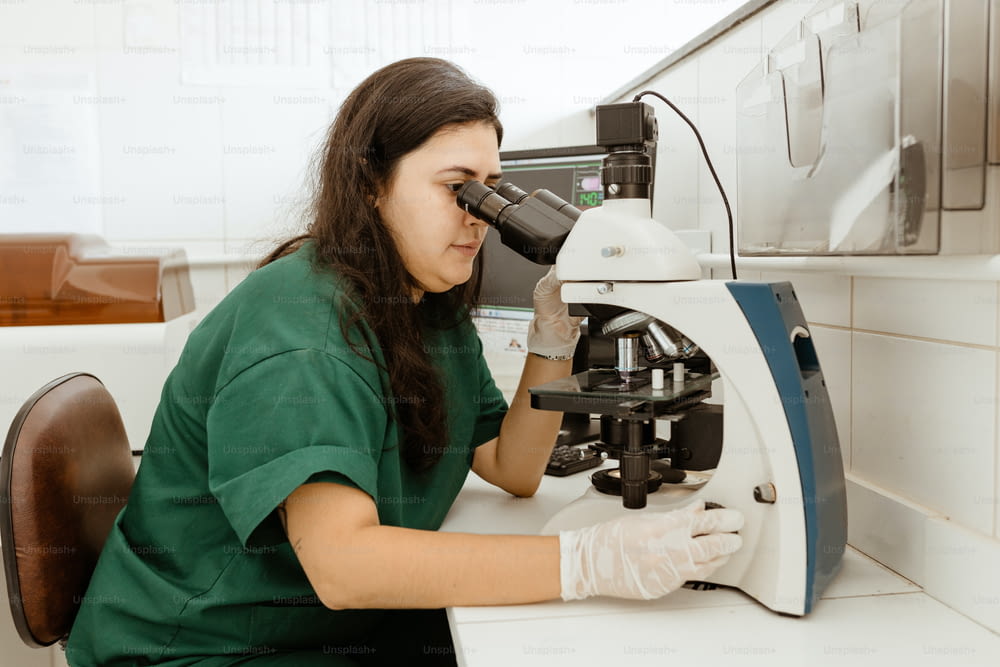 Una mujer con una camisa verde mirando a través de un microscopio