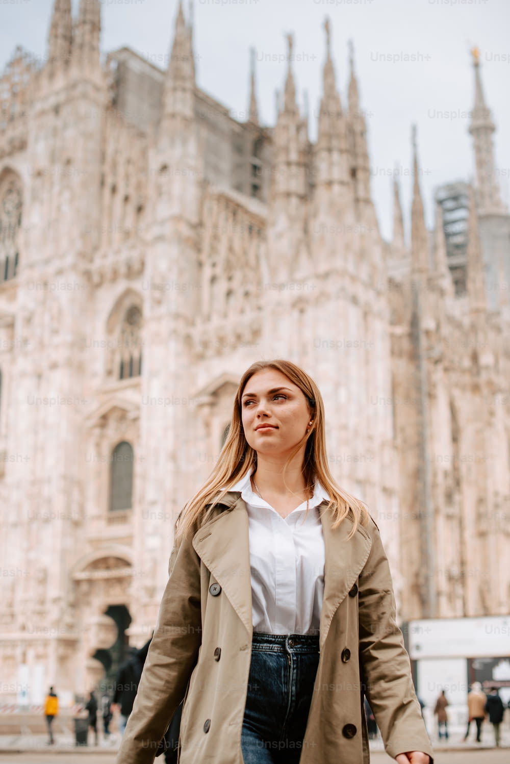 a woman in a trench coat is standing in front of a cathedral