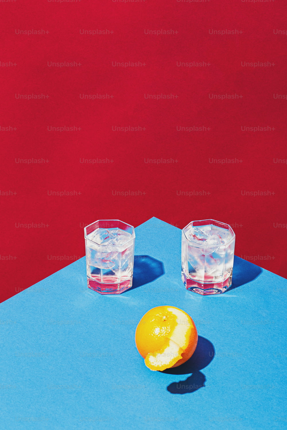 two glasses of water and an orange on a blue surface