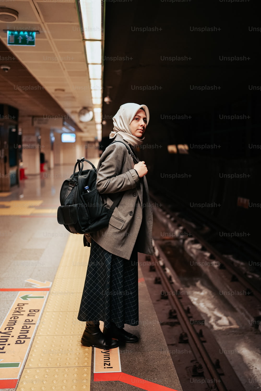 a woman standing on a train platform with a backpack