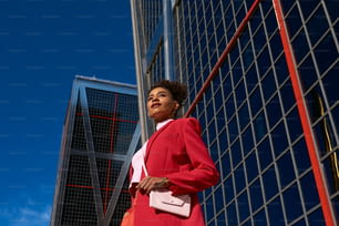 고층 건물 앞에 서 있는 빨간 양복을 입은 여자