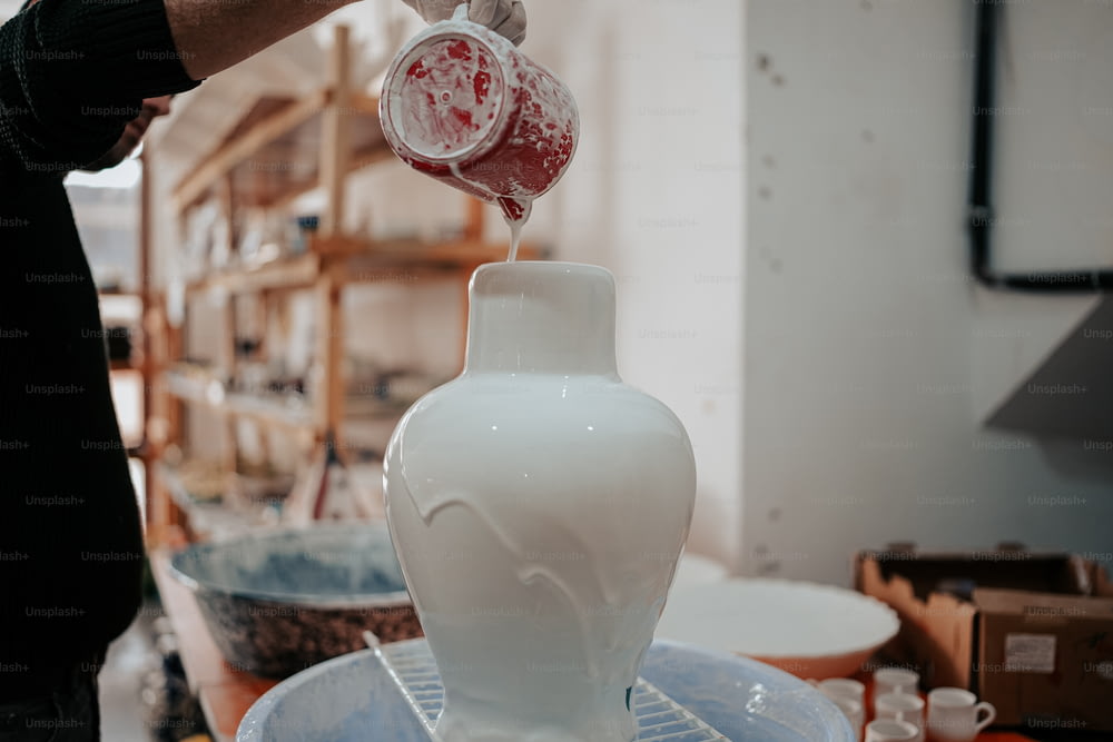 a person pouring something into a white vase