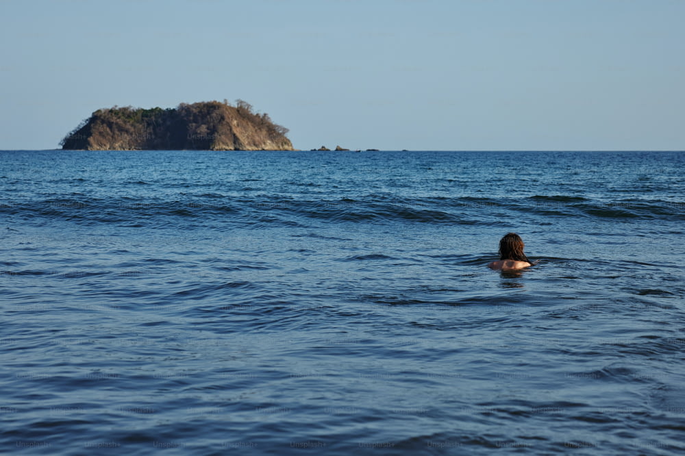 uma pessoa nadando no oceano com uma pequena ilha ao fundo