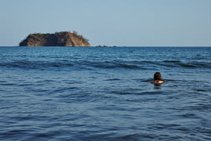 a person swimming in the ocean with a small island in the background