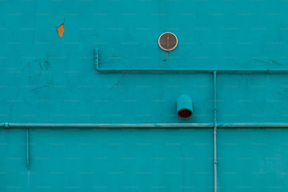 a blue wall with pipes and a vent on it